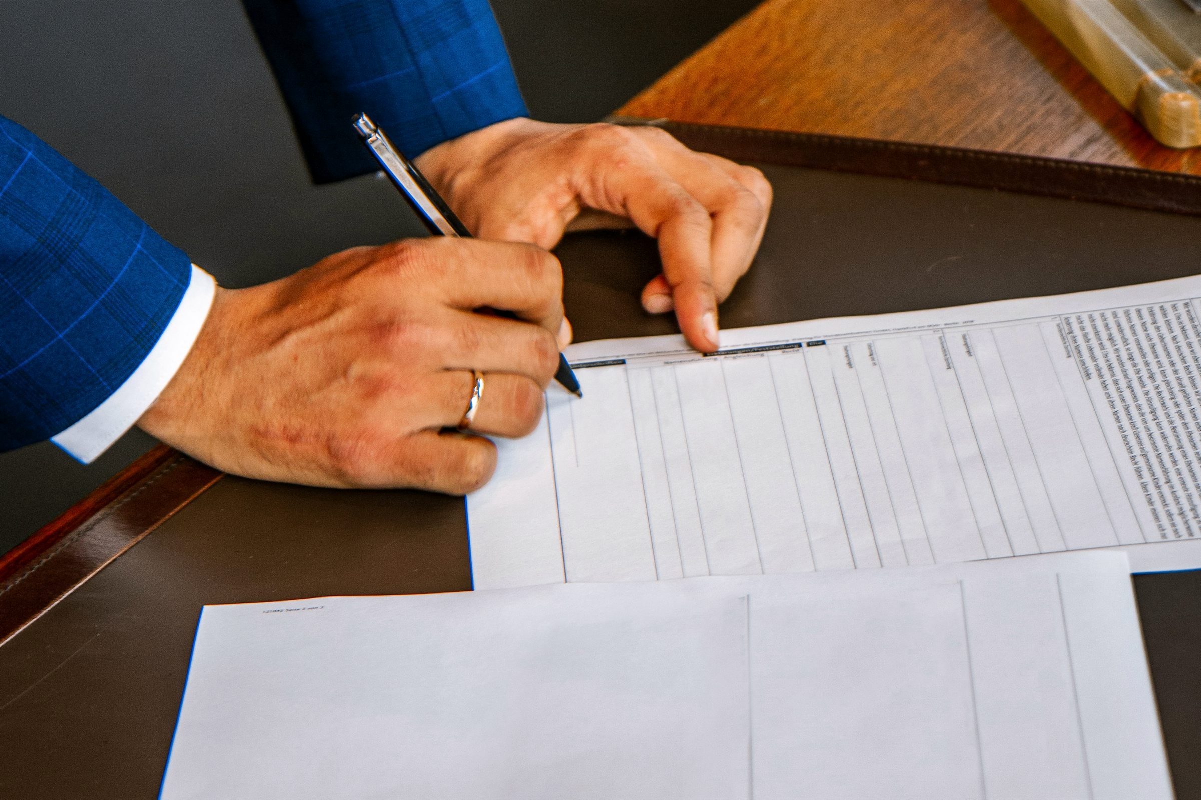 Hands in a navy suit signing printed forms on a desk